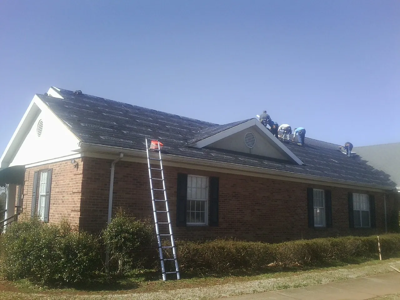 Crew tearing shingles off a brick ranch roof with a ladder set — Metal Roof Repair work by our crew in Ulmer