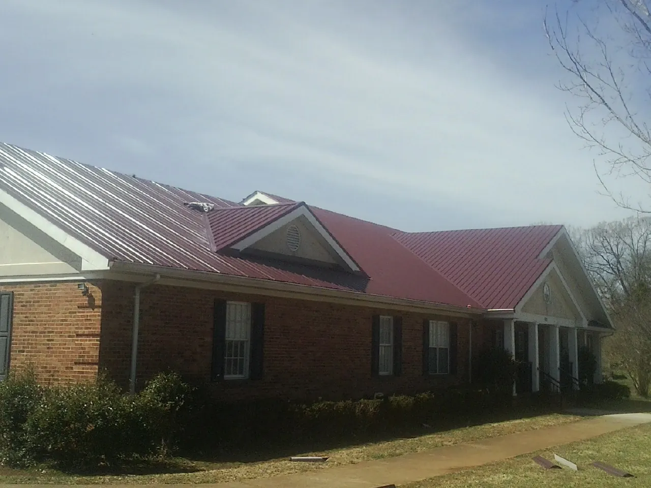 Red metal roof with gabled entries on a long brick building, from a Hail Damage Roof Repair job in Ulmer