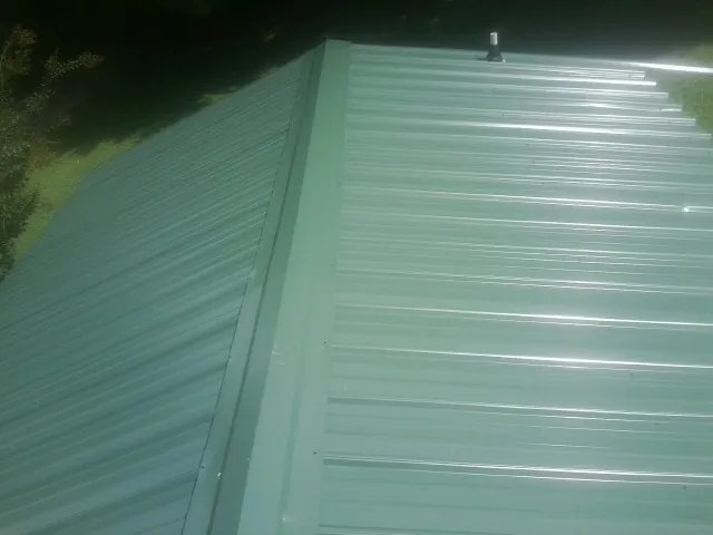 New green metal panels meeting at the ridge of a roof — Flat Roof Repair work by our crew in Ulmer