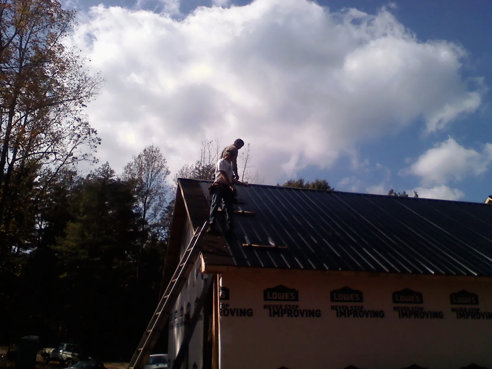 Roofer fastening dark metal panels high against a cloudy sky, from a Roof Inspection job in Ulmer